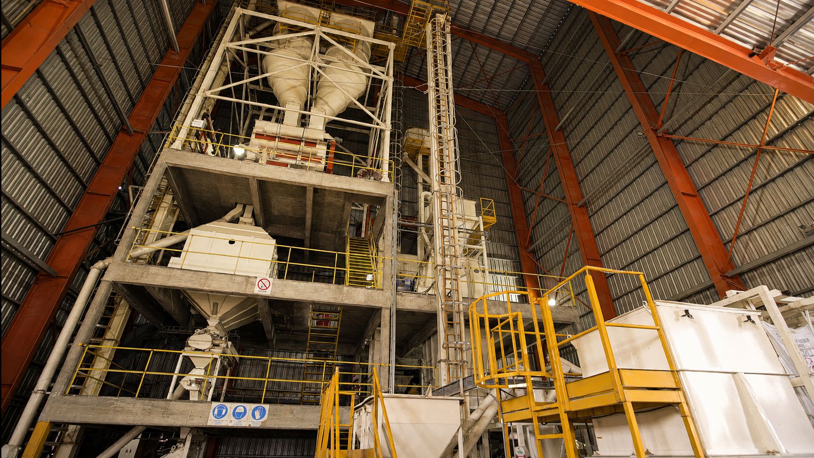 Interior de una planta de alimento balanceado: torre de proceso de hormigón, tolvas y pasarelas con barandas amarillas